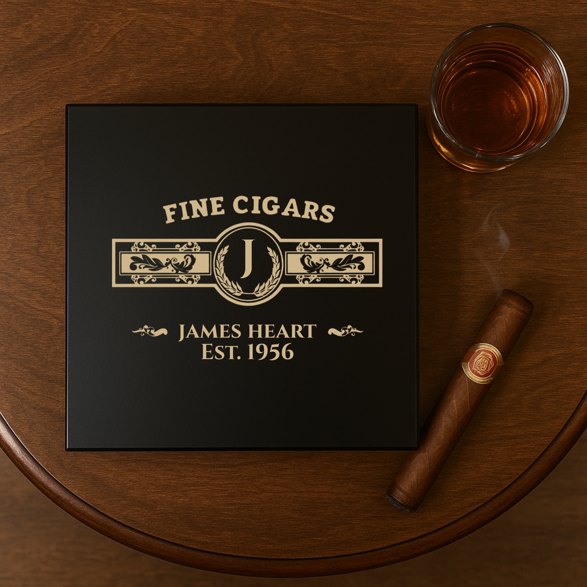Black cedar humidor with gold engraving reading "FINE CIGARS," decorative initial "J," "JAMES HEART," and "EST. 1956," displayed with a cigar and whiskey glass