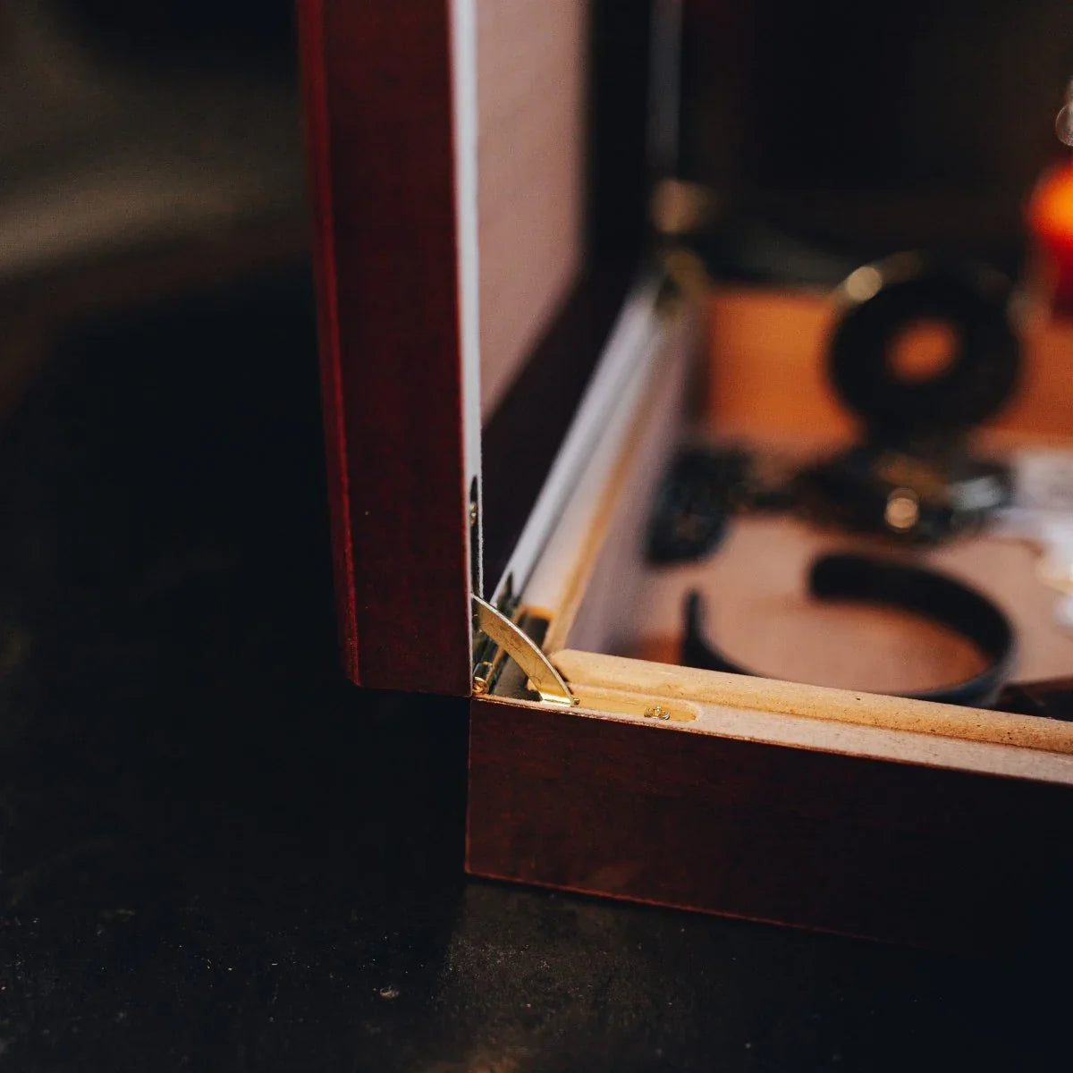 Close-up detail of dark wood humidor edge showing brass hinge and natural cedar lining interior with blurred cigar storage visible in background